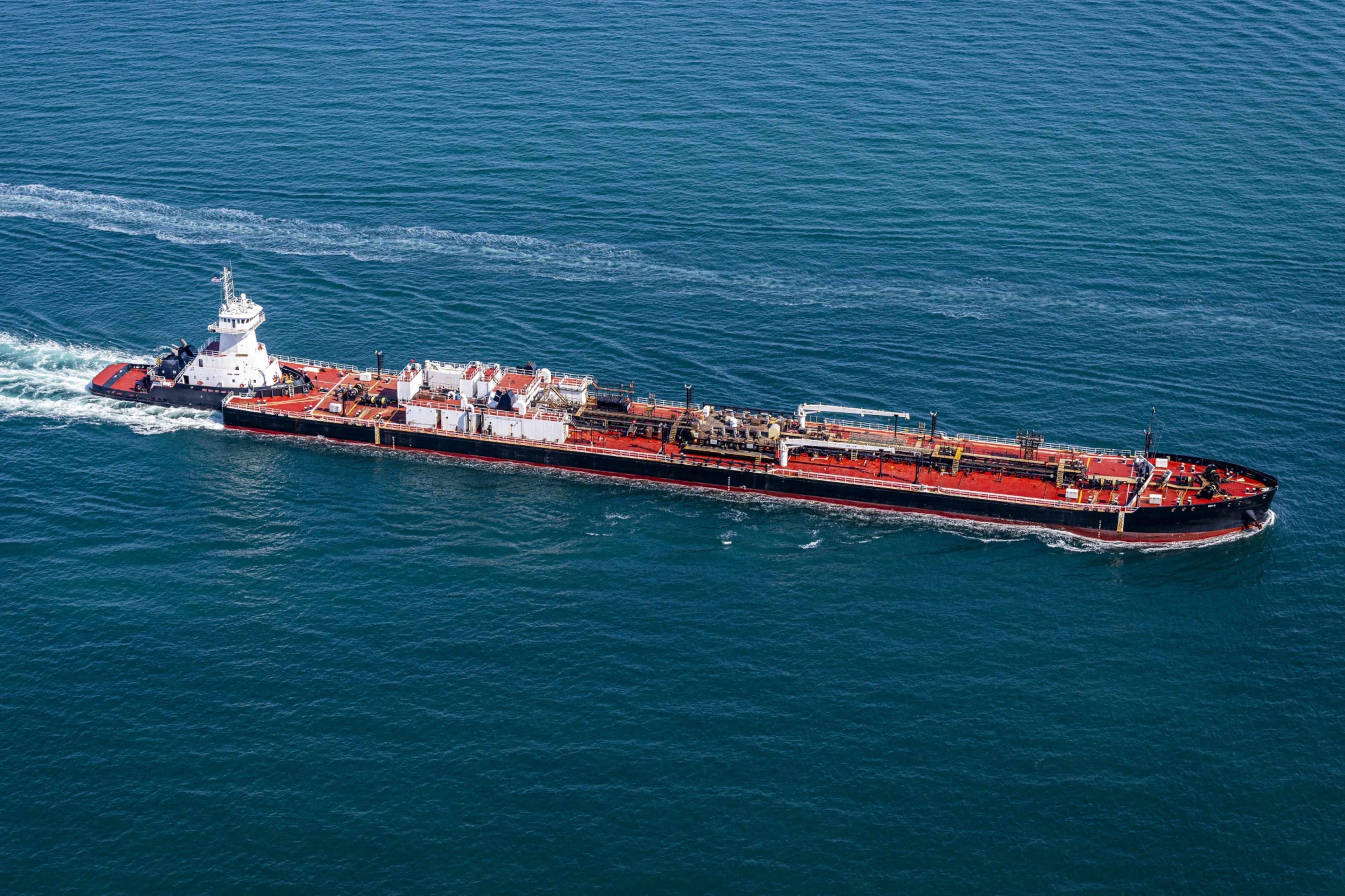 A large oil tanker ship travels across deep blue ocean water, leaving a wake behind it.